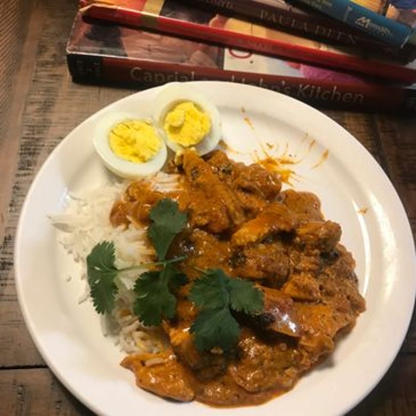 Chicken curry with white rice, fresh cilantro, and hard-boiled eggs on a white plate.