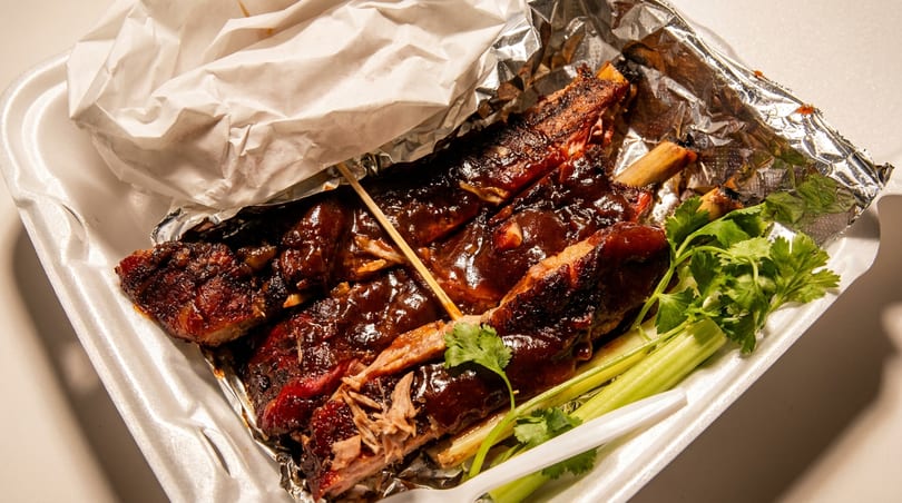 Sticky BBQ ribs with celery and cilantro in a styrofoam takeout container.
